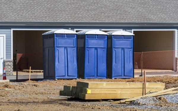Three portable toilets lined up outside a home under construction